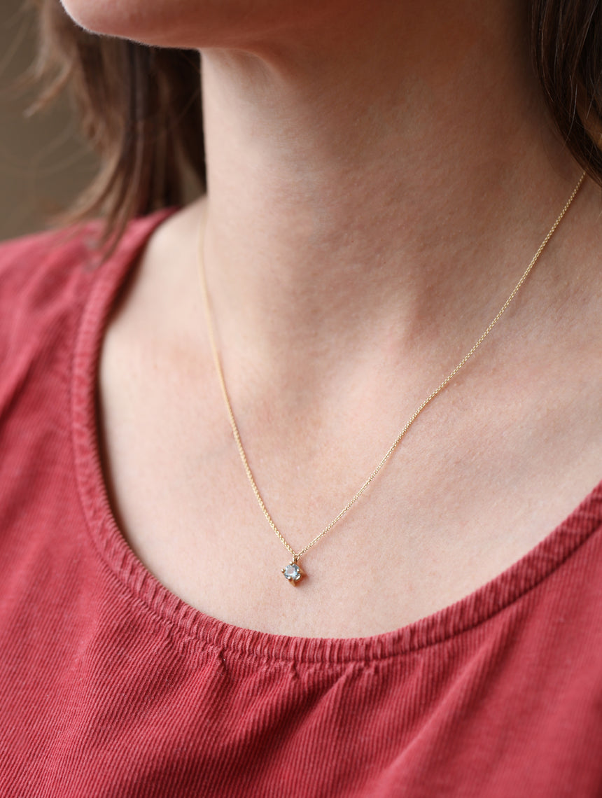 Gold necklace with a small pendant worn by a person in a red top.