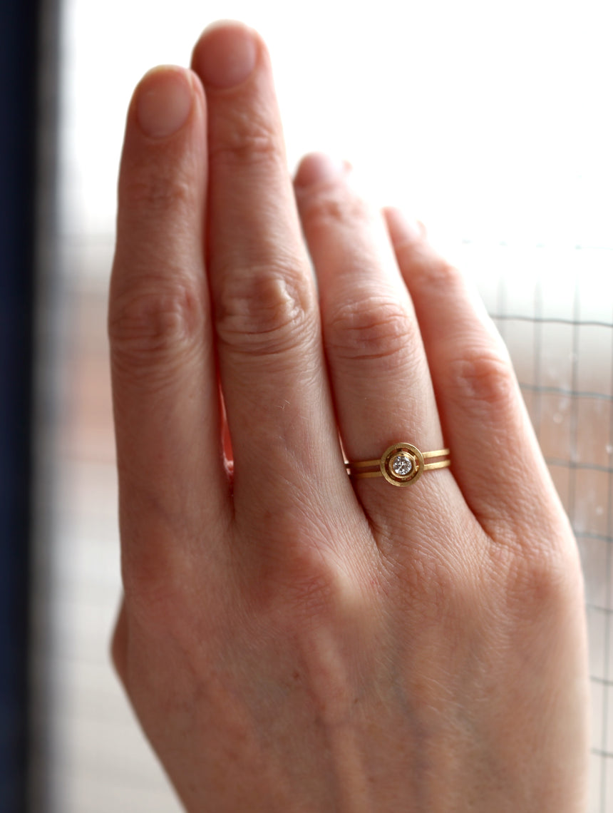 Solitaire ring with circular detail eith central diamond. 18ct yellow gold, textured finish. Worn on hand.
