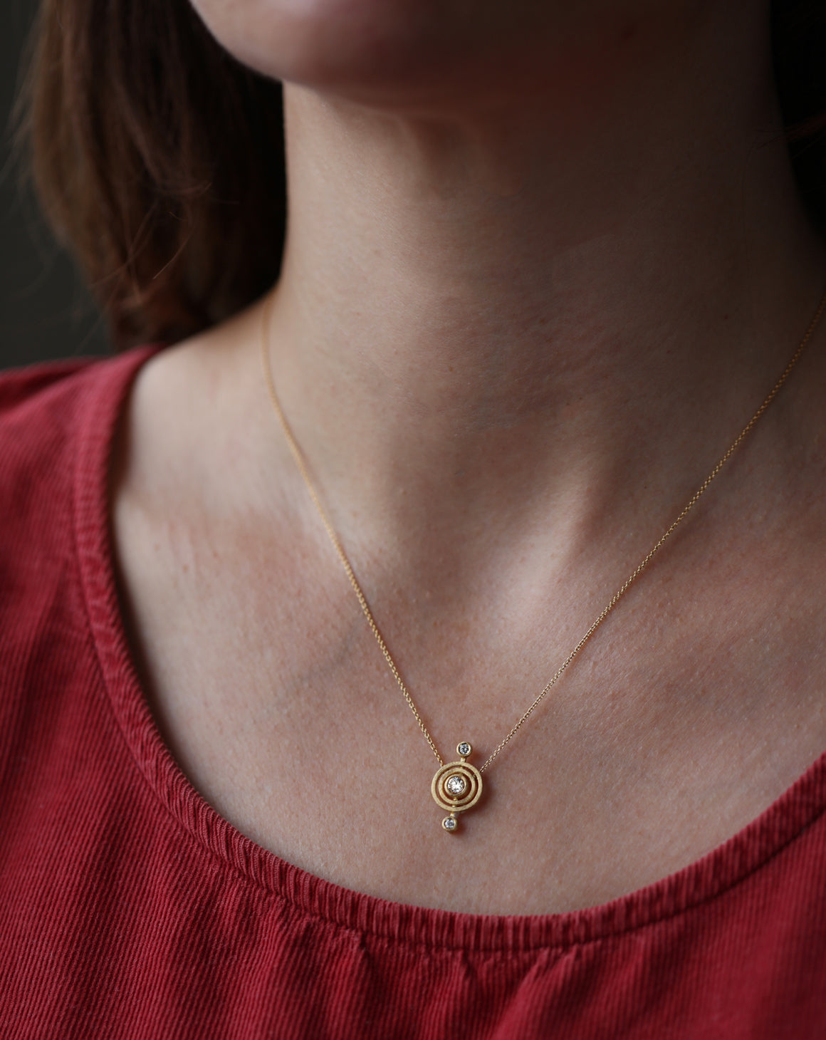 Geometric pendant with circular detail and three white diamonds. 18ct yellow god, textured finish. Worn on neck.