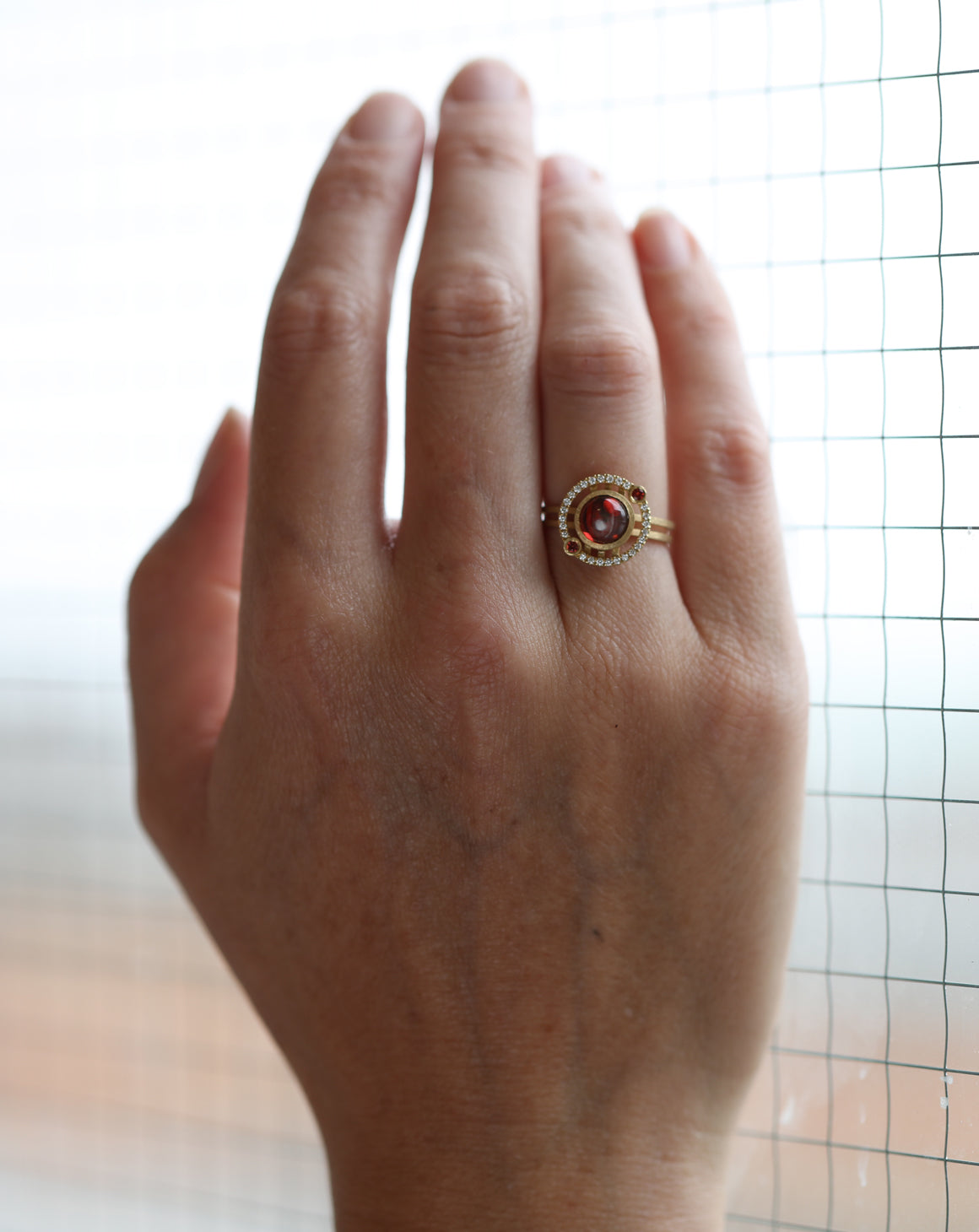 Geometric ring with red garnet and two orange sapphires and a diamond circular surround. 18ct yellow gold, textured finish. On hand.