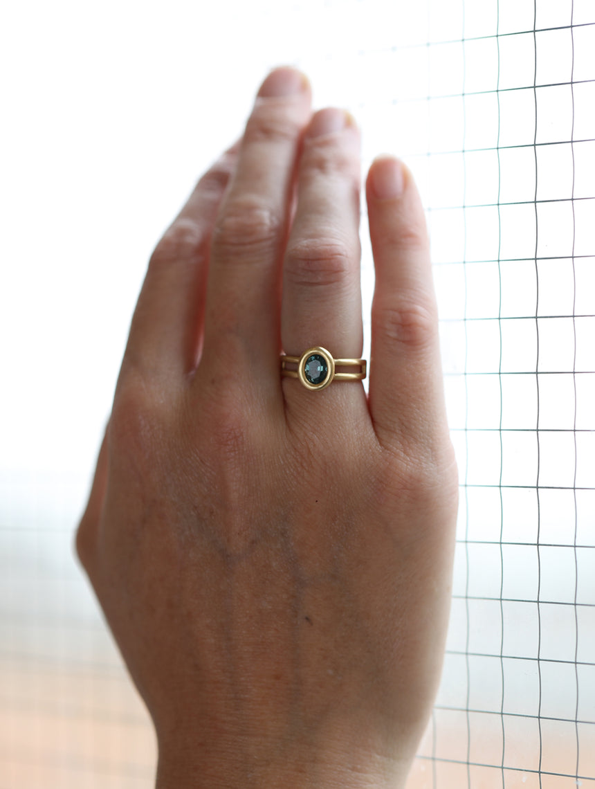 Solitaire ring with oval teal sapphire and double band. 18ct yellow gold, satin finish. On hand.