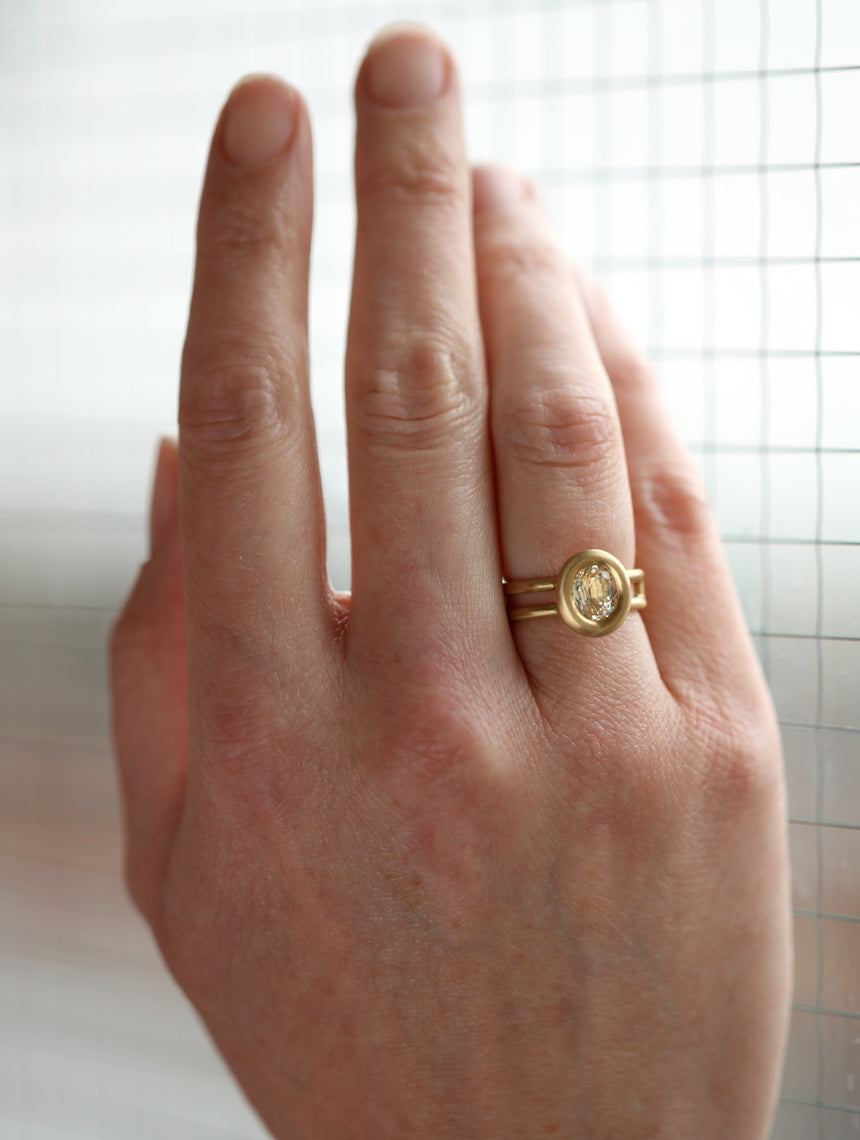 Oval pale yellow sapphire ring with a heavy rounded bezel setting and double band. 18ct yellow gold, satin finish. On hand.