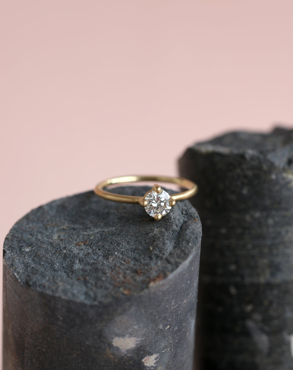 Solitaire ring with round white diamond, four claw setting. 18ct yellow gold, satin finish. On rock.