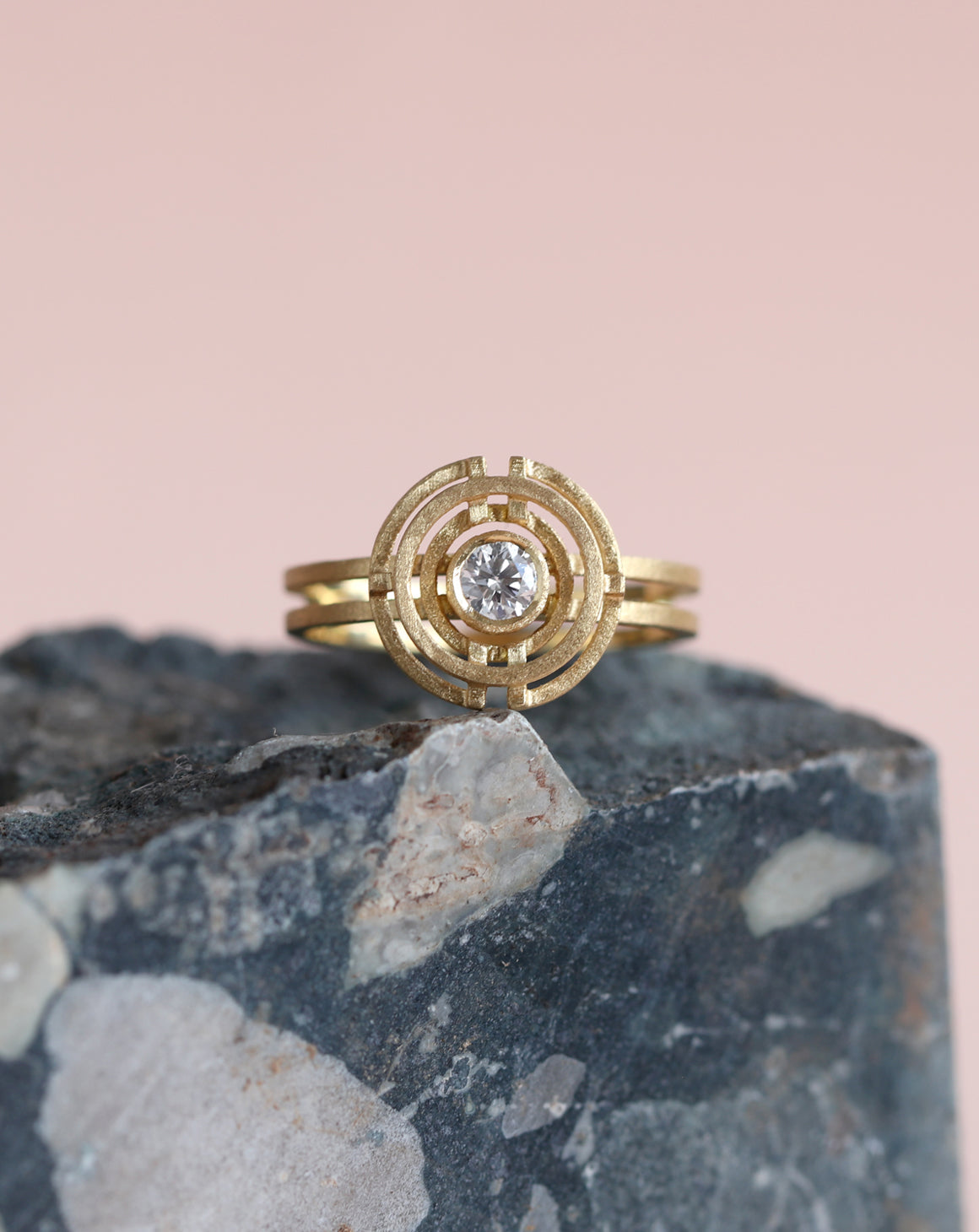 Geometric ring with circular detail and central white diamond. 18ct yellow gold, textured finish. On rock.