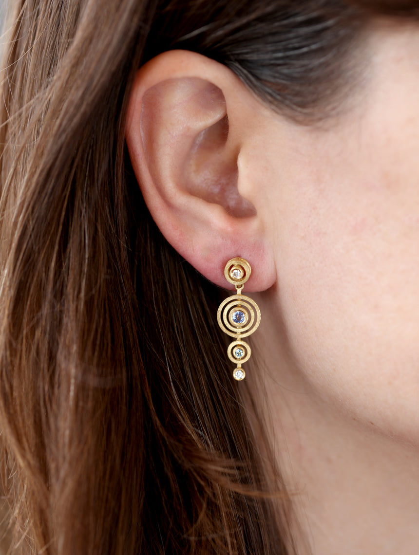Drop earrings with concentric circular detail, set with blue sapphire, green beryl and white diamond. Textured 18ct yellow gold. Worn in ear.