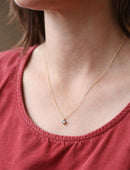 Gold necklace with a small pendant worn by a person in a red top.