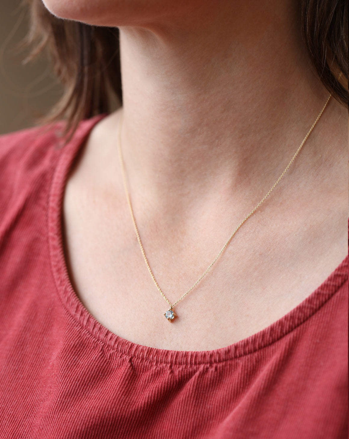 Gold necklace with a small pendant worn by a person in a red top.