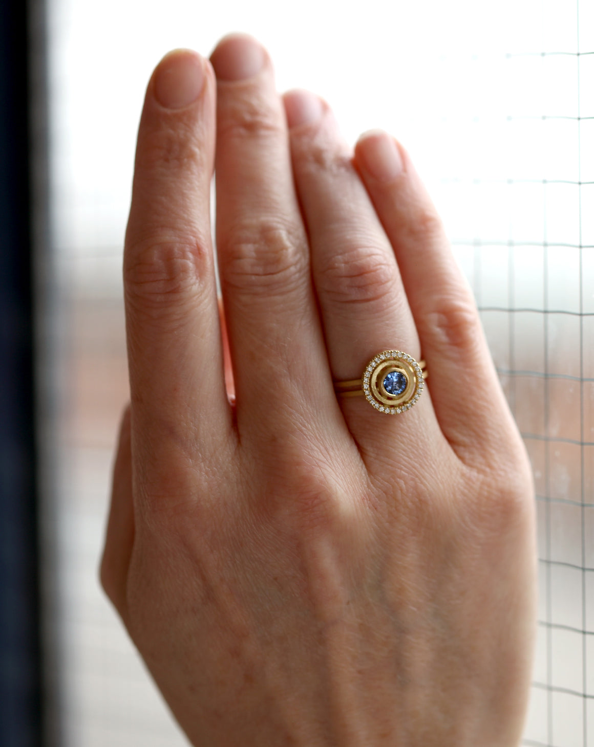 Blue sapphire ring with diamond halo detail. Textured 18ct yellow gold. On hand.