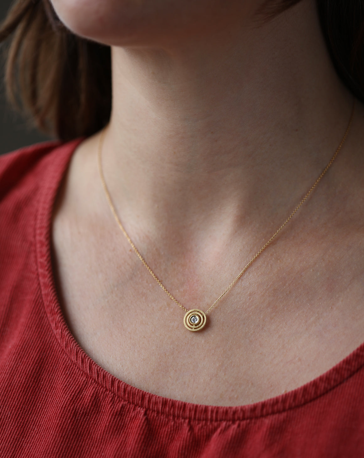 Geometric pendant with concentric circle detail, with central diamond. 18ct yellow gold, textured gold. Worn on neck.