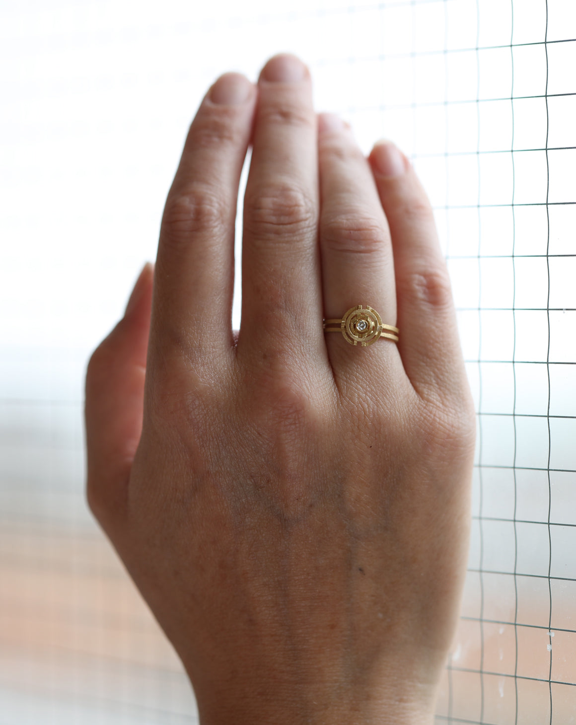 Geometric ring with concentric circle detail, with central diamond, double band. 18ct yellow gold, textured gold. On hand,