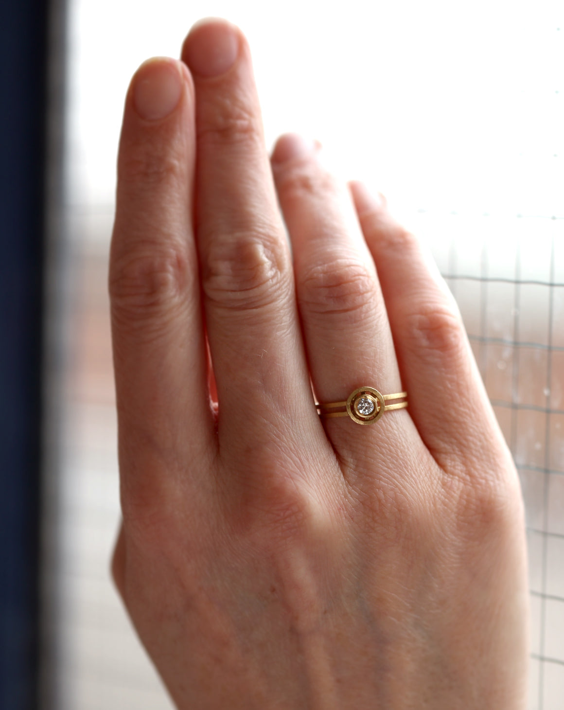 Solitaire ring with circular detail eith central diamond. 18ct yellow gold, textured finish. Worn on hand.