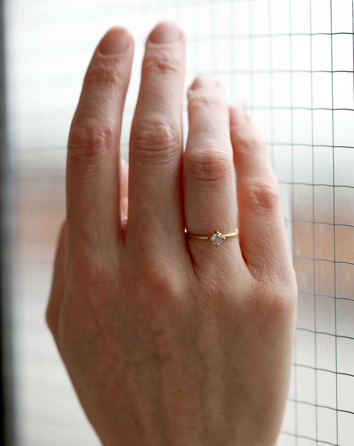 Solitaire ring with round white diamond, four claw setting. 18ct yellow gold, satin finish. Worn on hand.
