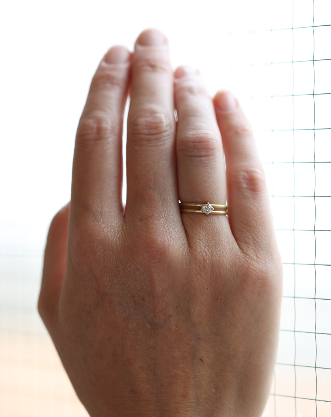 Solitaire ring with round white diamond and double band. 18ct yellow gold, satin finish. On the hand.