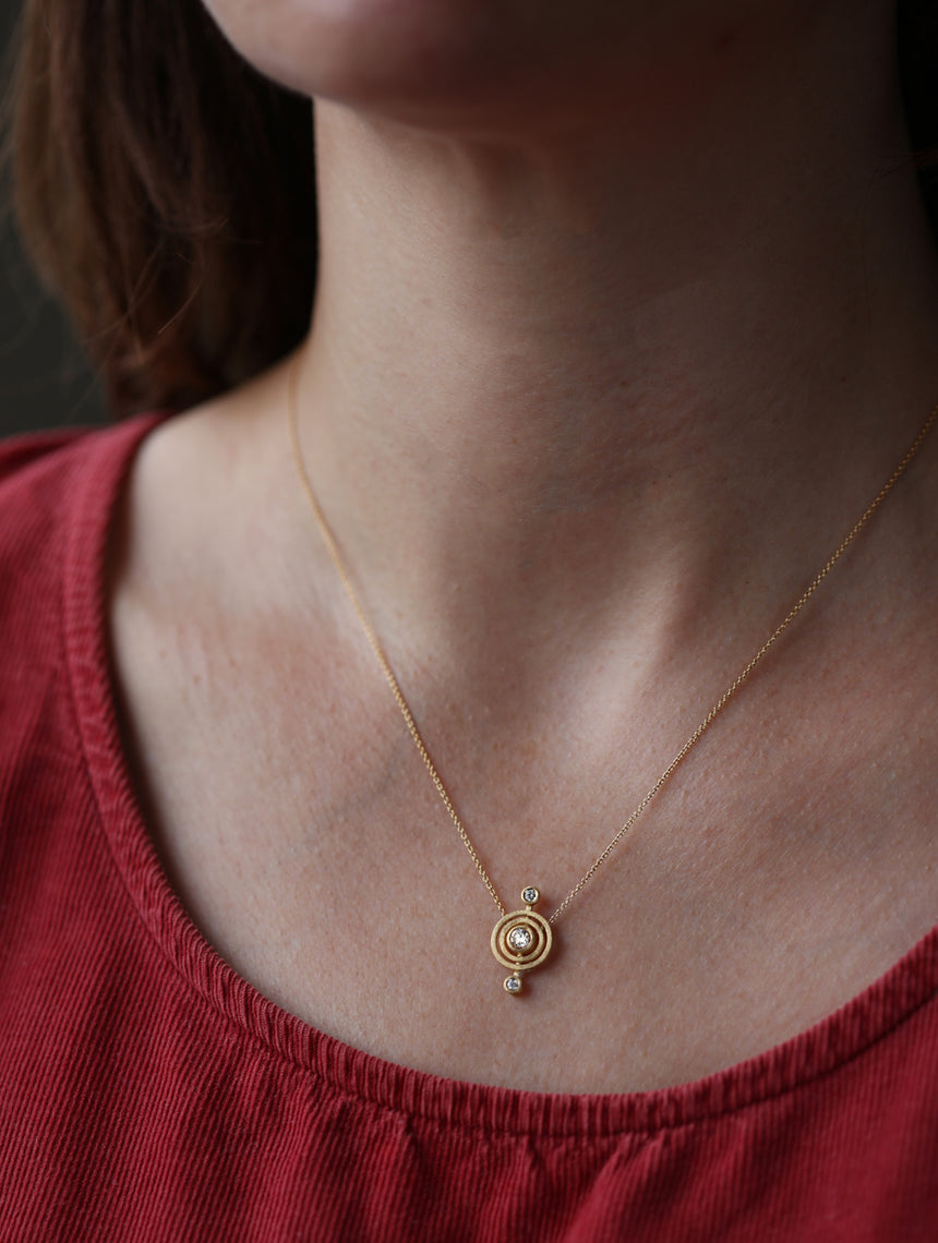 Geometric pendant with circular detail  and three white diamonds. 18ct yellow god, textured finish. Worn on neck.