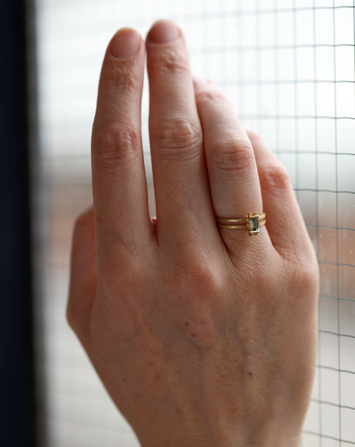 Rectangle green sapphire ring with geometric setting and double band. 18ct yellow gold, textured finish. On hand.