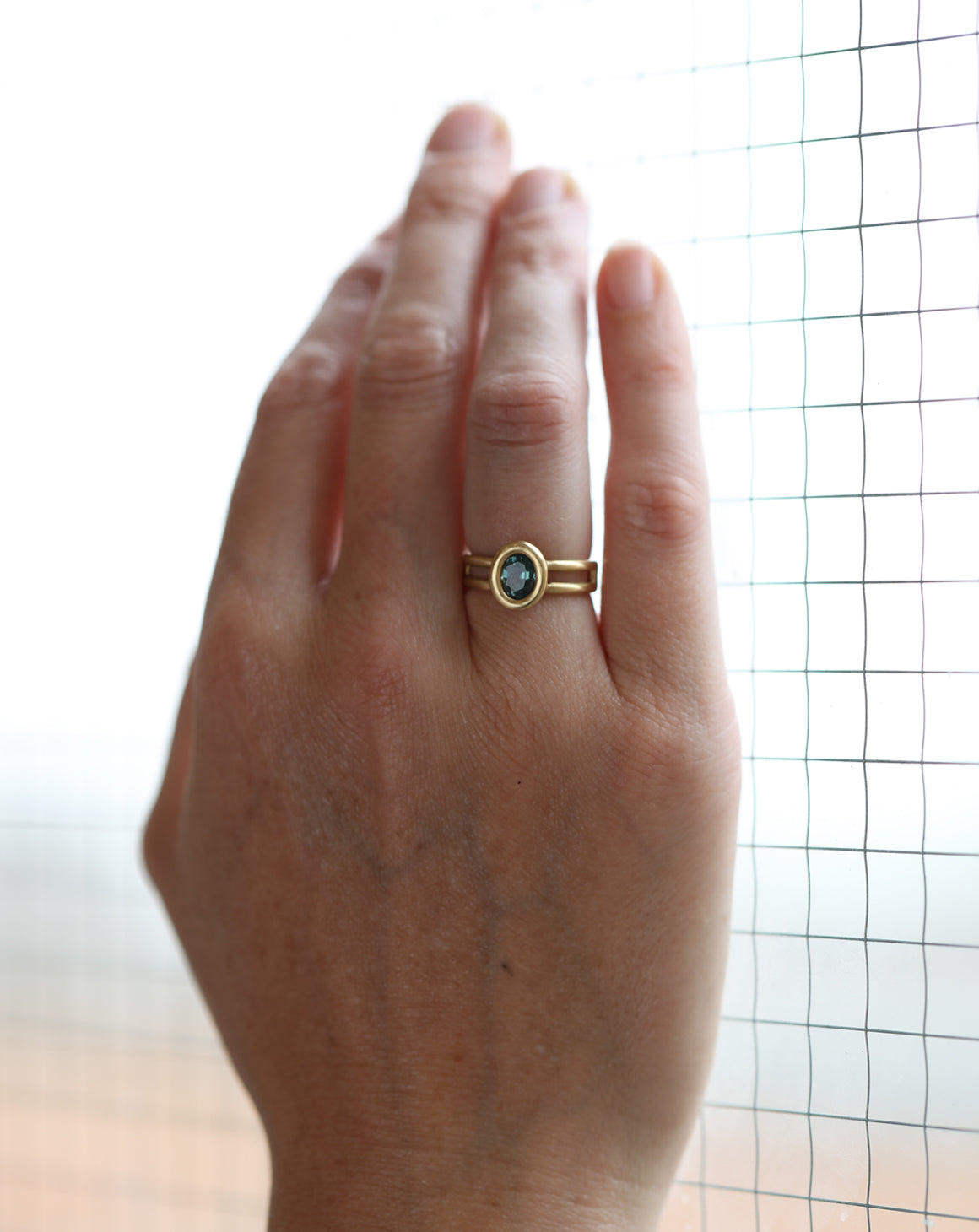 Solitaire ring with oval teal sapphire and double band. 18ct yellow gold, satin finish. On hand.