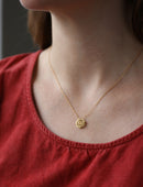 Geometric pendant with concentric circles surrounding yellow sapphire. 18ct yellow gold, textured finish. On neck.