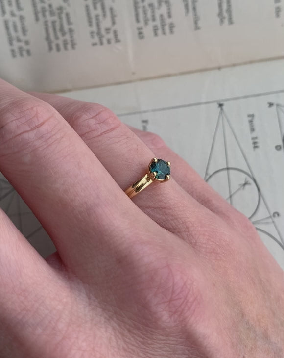 Solitaire ring with teal sapphire and double band. 18ct yellow gold, polished finish. On hand.