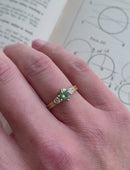 Three stone ring with green sapphire and white diamonds. Joined double band, 18ct yellow gold satin finish. On hand.
