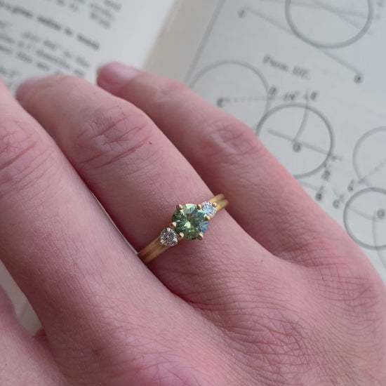 Three stone ring with green sapphire and white diamonds. Joined double band, 18ct yellow gold satin finish. On hand.