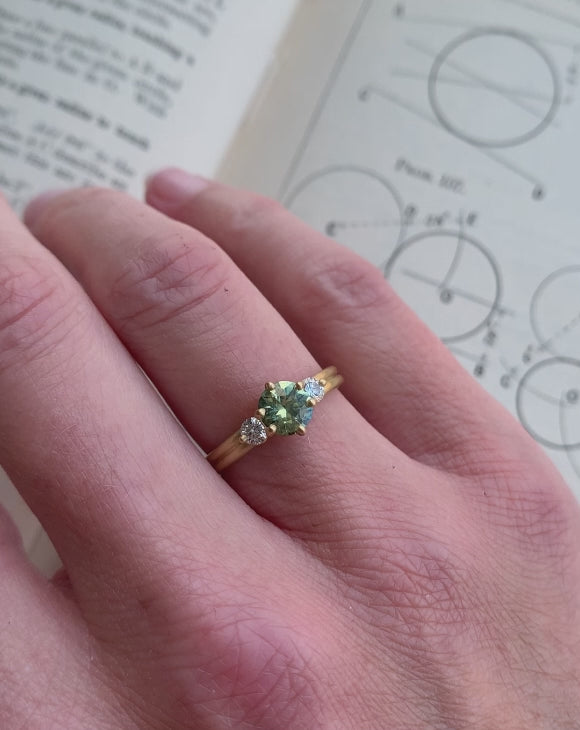 Three stone ring with green sapphire and white diamonds. Joined double band, 18ct yellow gold satin finish. On hand.