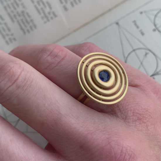 Statement ring made from concentric circles. Central blue sapphire surrounded by 18ct yellow gold rings. On hand.