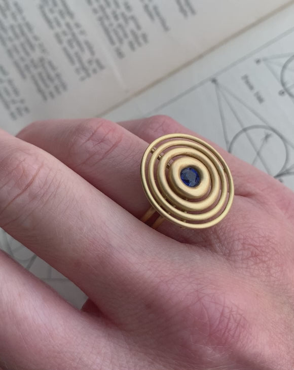 Statement ring made from concentric circles. Central blue sapphire surrounded by 18ct yellow gold rings. On hand.
