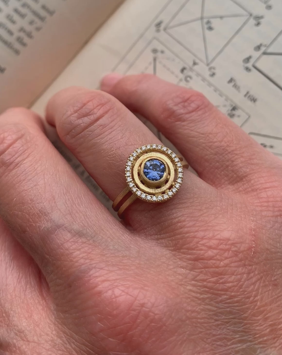 Blue sapphire ring with diamond halo detail. Textured 18ct yellow gold. On hand.